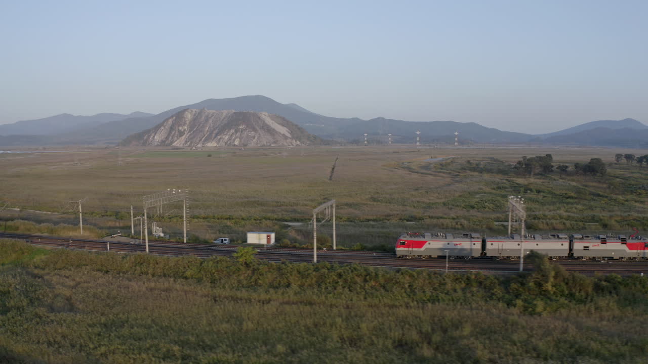 석양을 배경으로 산을 배경으로 푸른 들판을 가로지르는 긴 빈 석탄 객차 화물을 끄는 러시아 철도 열차 기관차, 러시아 연방
