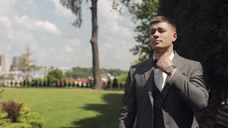 handsome groom in a suit and bow tie adjusting his tie outdoors