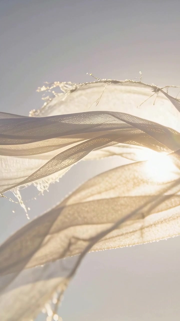 Vertical video: Waving sheer scarf with wind lifting layers showing sun over blue sky