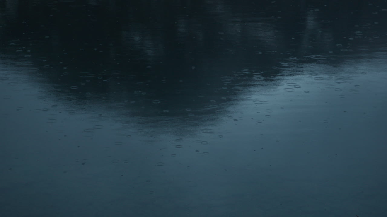 Gocce di pioggia che cadono nell'acqua al rallentatore, mostrando le gocce con una montagna che si riflette nell'acqua