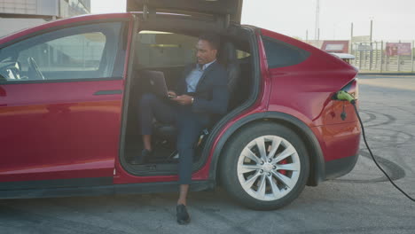 hombre de negocios trabajando en una computadora portátil dentro de un coche eléctrico