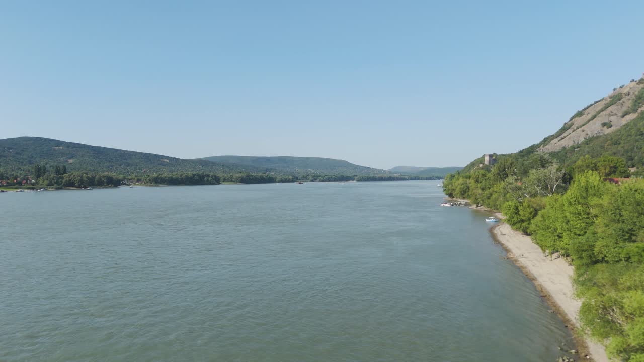Danube river flows through the Visegrad landscape, showing hills and shoreline under clear sky. Aerial, push forward