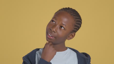 Studio-Portrait-Of-Young-Boy-Thinking-Against-Yellow-Background-