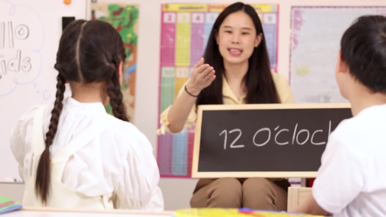 明るい教室で、小学校の先生が黒板を使って子どもたちに12時を指す時計の読み方を笑顔で教えています。