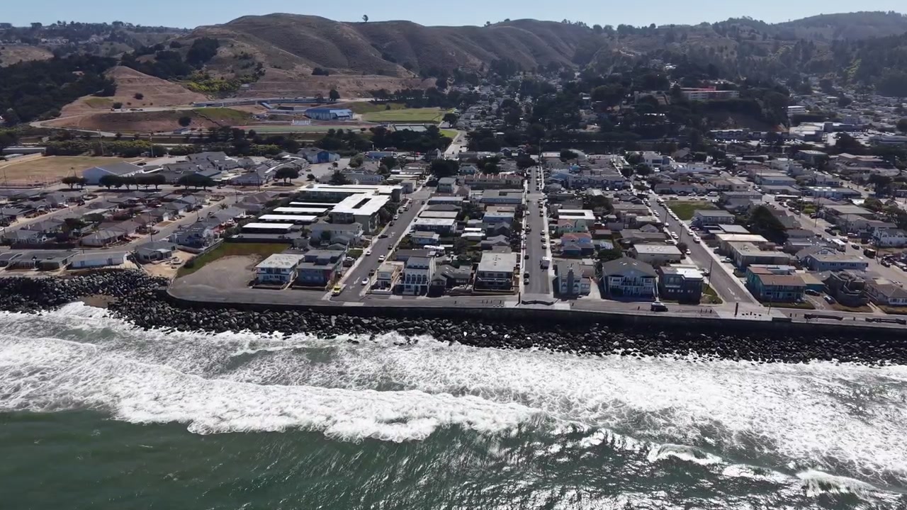 Prospettiva aerea che sorvola la pittoresca città costiera di Pacifica, California, rivelando le vaste onde dell'oceano che si infrangono contro la costa rocciosa e il paesaggio urbano