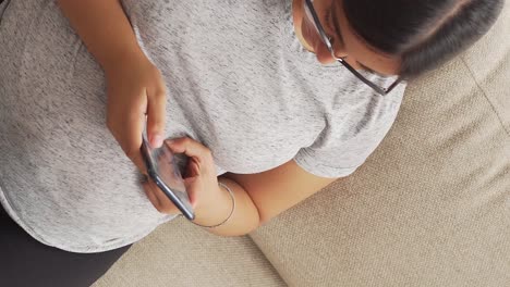 mujer embarazada morena con gafas sentada escribiendo en un teléfono móvil