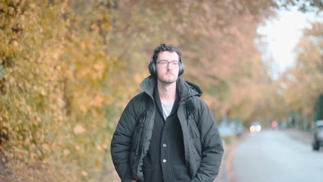 stylish european man with a beard and glasses leisurely strolls the autumnal suburbs of munich, deeply immersed in melodies from his headphones, absorbing the seasonal tranquility