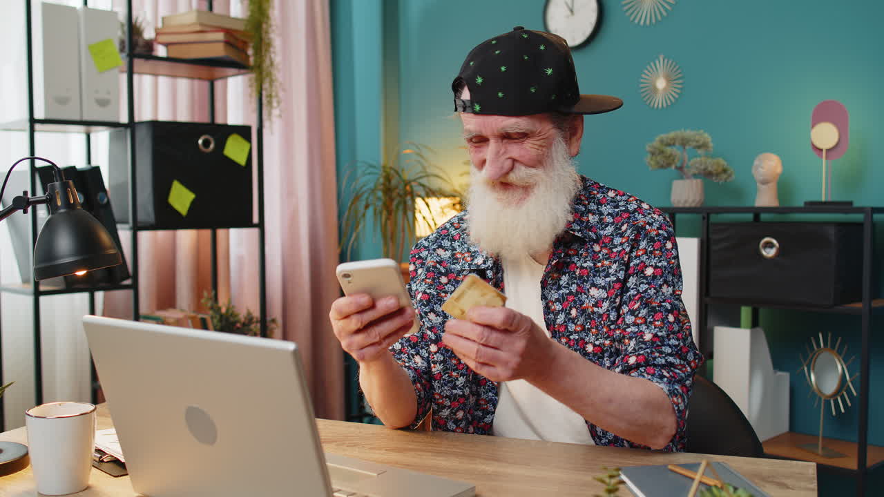 Happy senior man using bank credit card and laptop for online shopping payments at home office