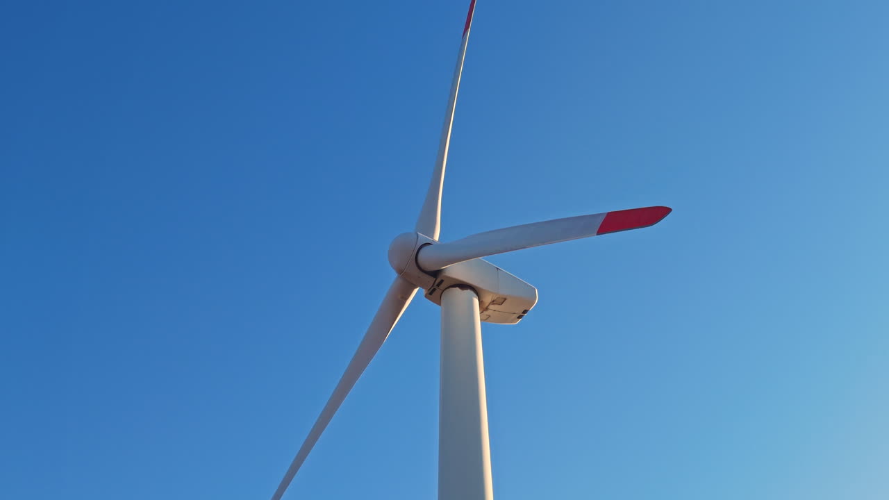 Aerogenerador que se alza bajo un cielo azul y despejado por la tarde, capturando energía del fuerte viento para la generación de energía renovable en una zona rural