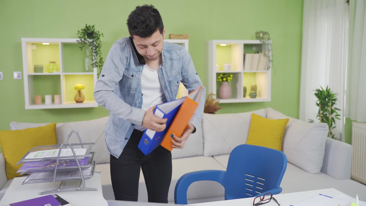 joven torpe distraído que trabaja remotamente en casa deja caer archivos de papeleo de su mano.