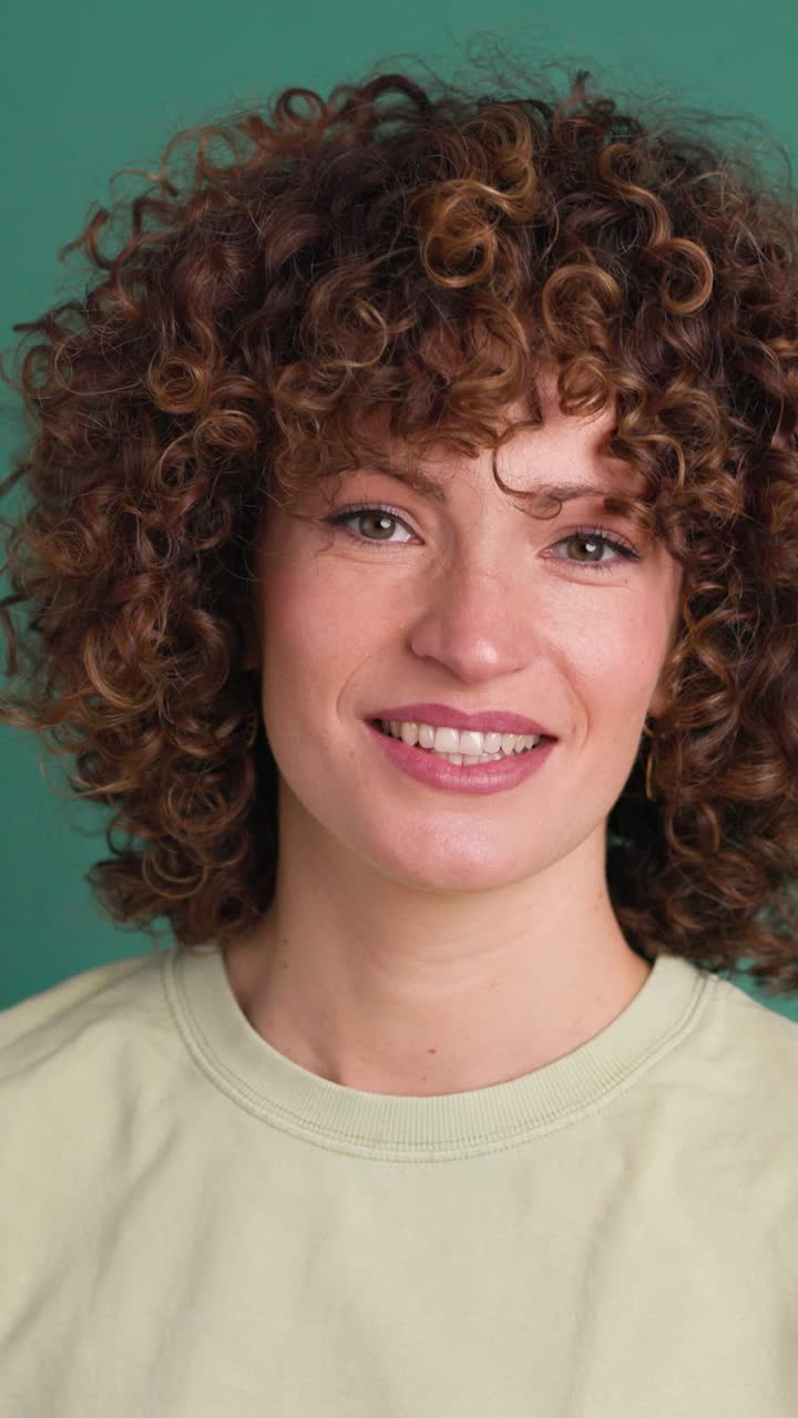 Smiling standing young curly haired woman on green background. Vertical orientation
