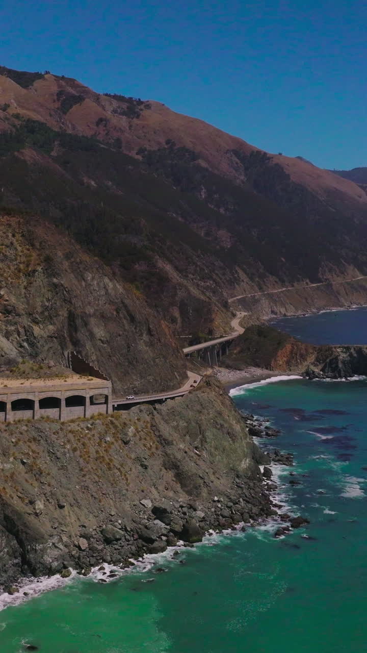 Rocky coastline of California with roads built on the mountains. Rocks shed covering the part of the highway from falling stones. Aerial view. Vertical video
