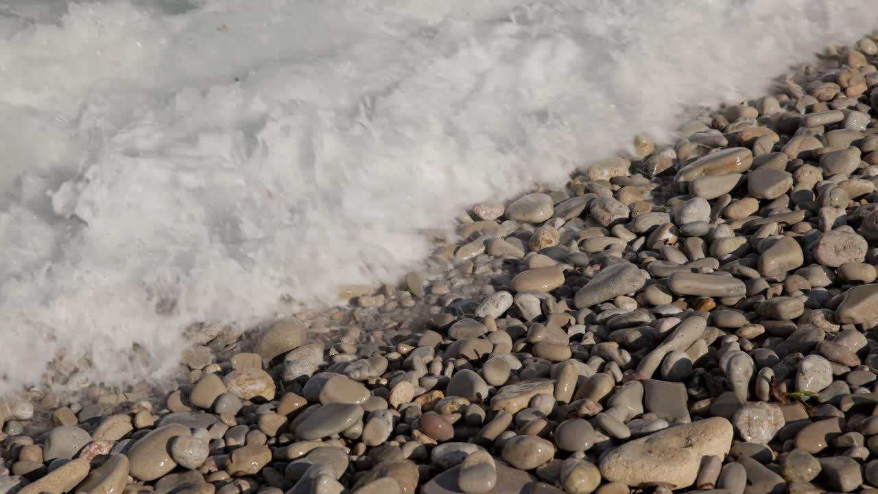 Clear shallow water with sunlight patterns over pebbles on Mallorca beach shore, therapeutic backdrop