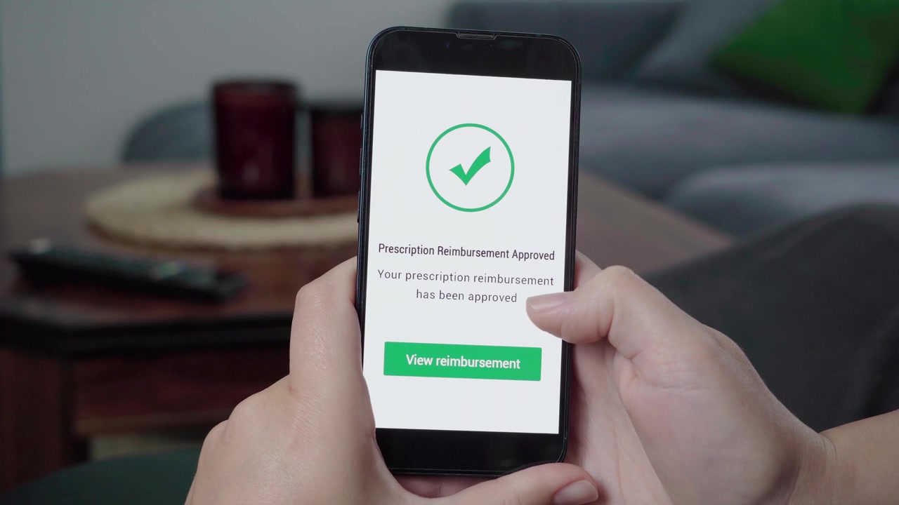 Primo piano di mani che utilizzano un'app di salute mobile che conferma l'approvazione di un rimborso per farmaci con una grande icona di spunta.