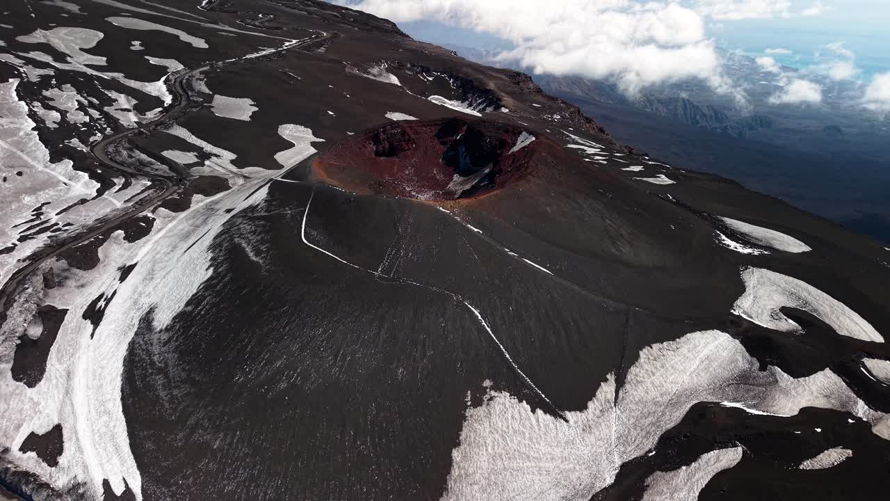Flygvy över Etna som reser sig över vulkankratern och snötäckt svart, bördig bergsmark.