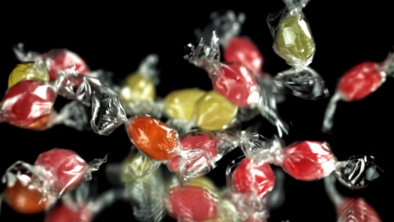 Caramelle colorate incartate che cadono e rimbalzano su una superficie nera riflettente al rallentatore