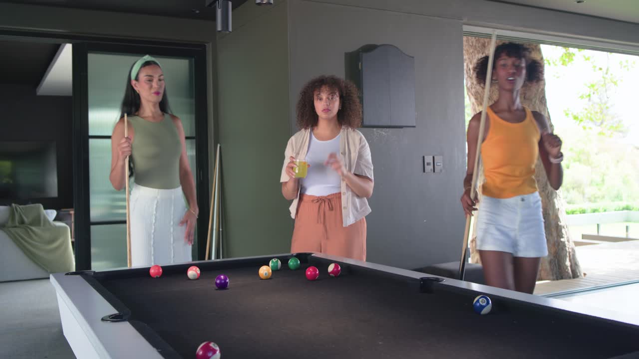 African American women, one in yellow top lining, striking cue ball while playing at pool table