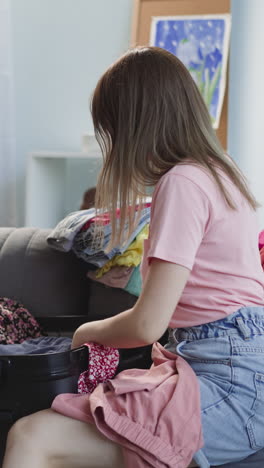 little son with straw hat puts toys into suitcase while mother gathers luggage in living room. woman with toddler boy before for summer vacation