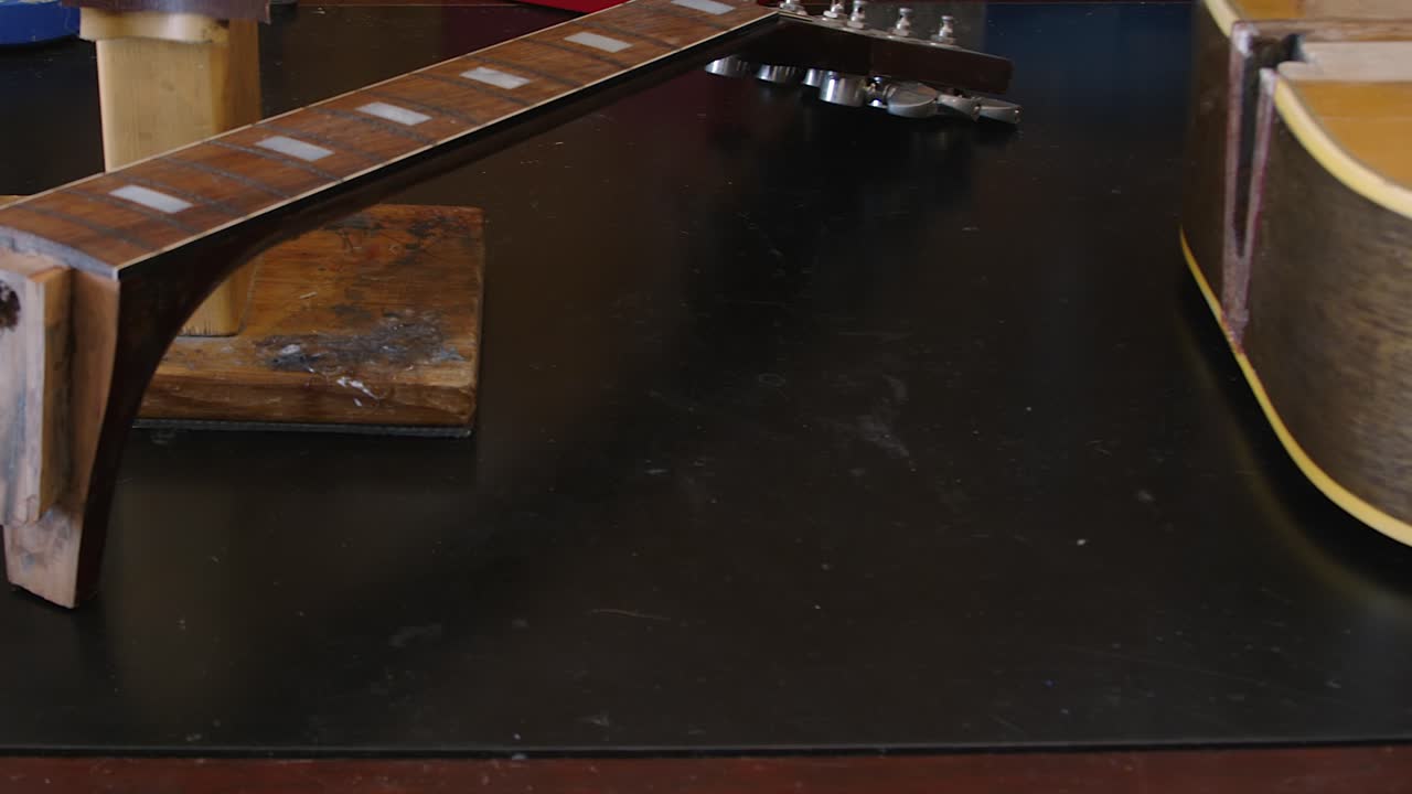 Perdeleri, sapı ve akustik gitar gövde parçalarıyla dolu çalışma tezgahı üzerinde kaydırma.
