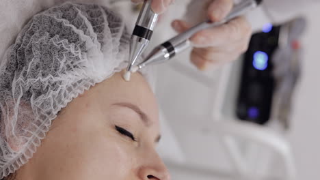 middle-aged woman receiving micro currents facial forehead skin treatment from beautician in salon