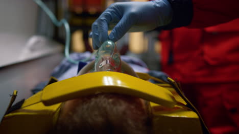 mano paramédica en guante sosteniendo una máscara de oxígeno en la cara del paciente en el coche de emergencia