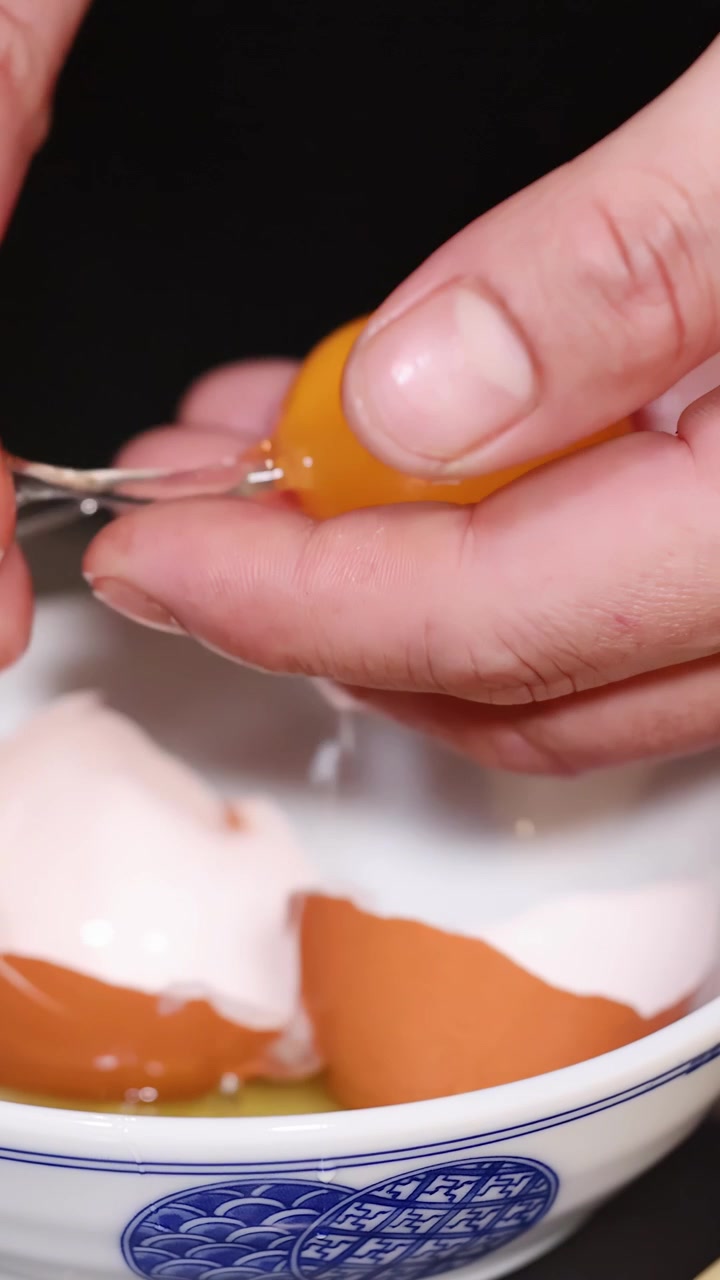 Close-up shot of hands carefully separating a raw egg yolk into a small glass bowl