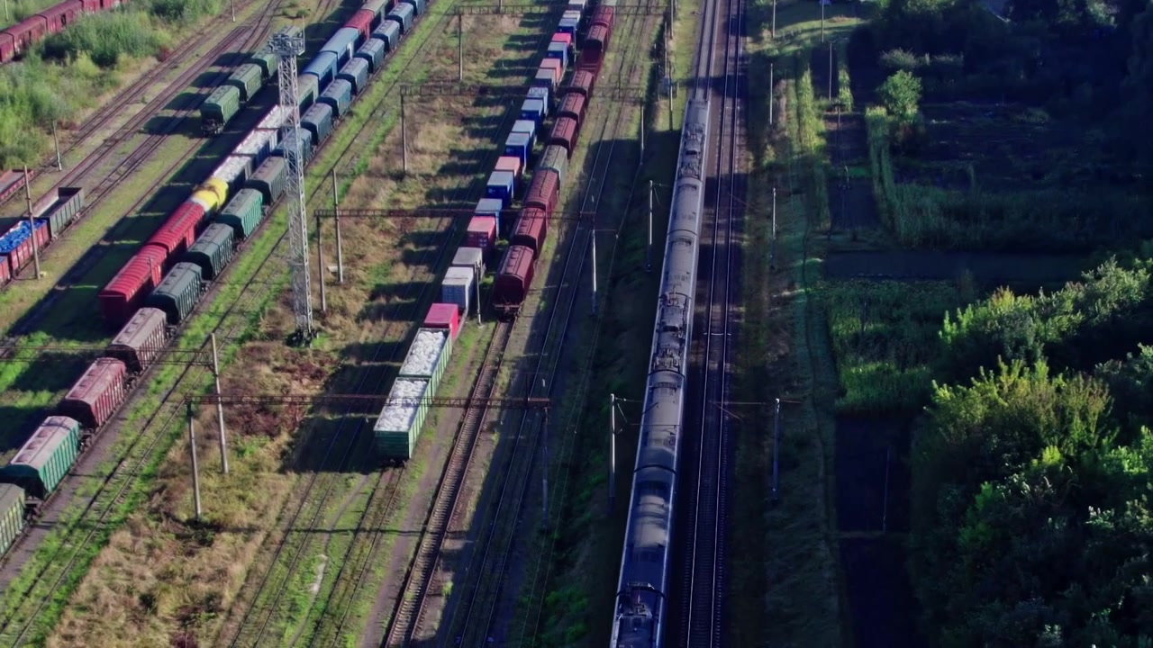 Treni che corrono sui binari accanto a uno scalo merci nel pomeriggio.