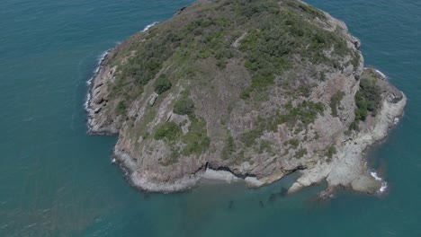 aerial, close up of bluff rock island with clear blue water in qld, australia