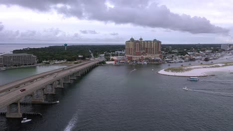 Vista-Aérea-De-Drones-Volando-Por-El-Costado-Del-Puente-De-Destin-Fl-Hacia-El-Pueblo-De-Harbourwalk-En-El-Puerto-De-Destin