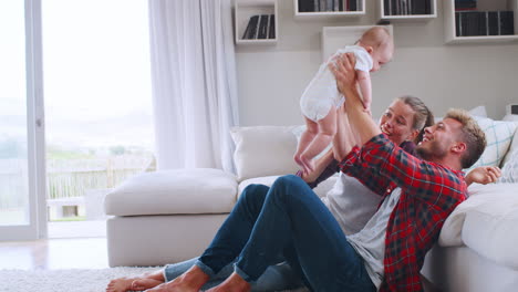 Young-white-couple-sit-playing-with-baby-at-home,-side-view