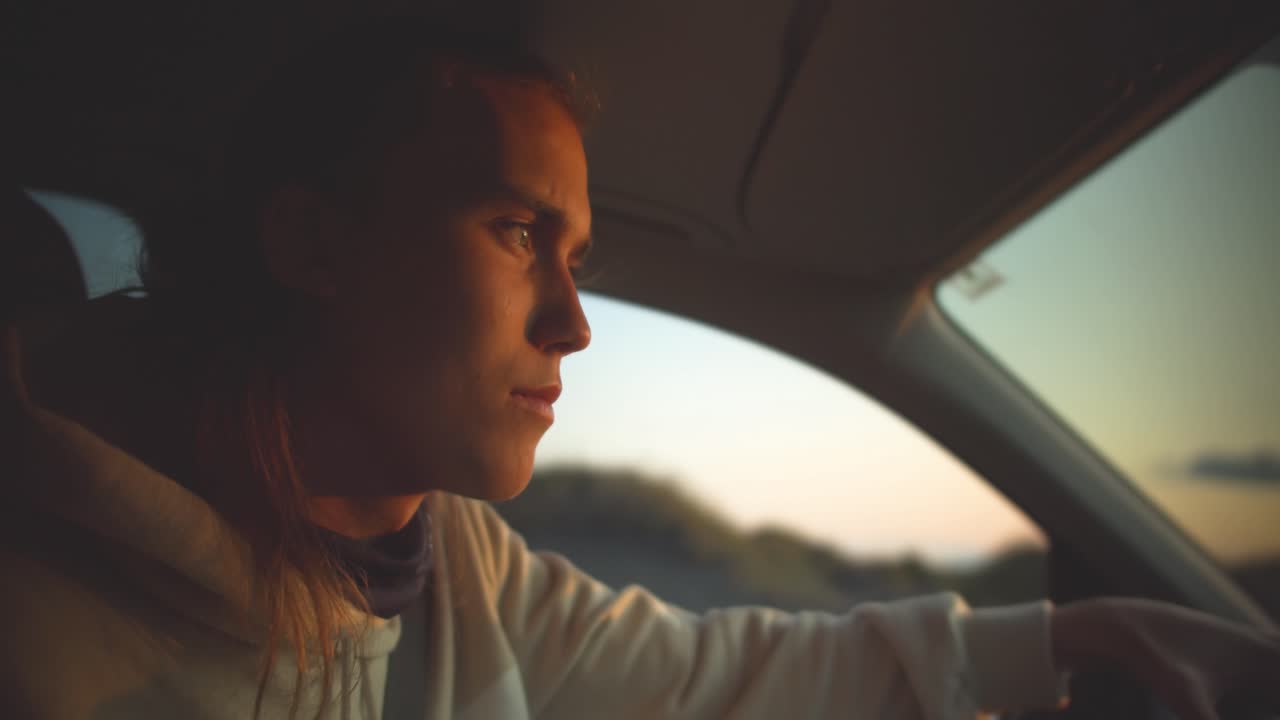 Young blond man is driving in the twilight of the setting sun in the car