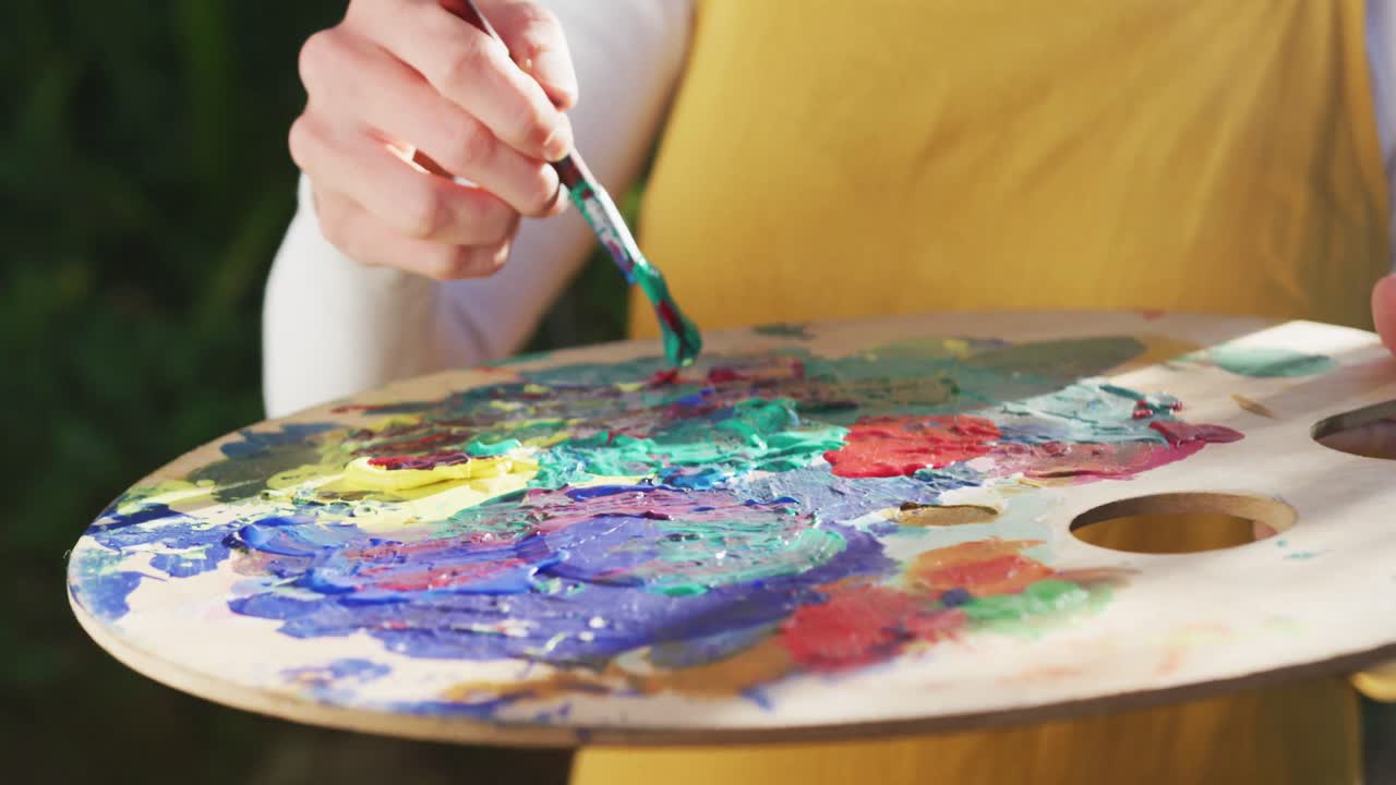 sección media de una mujer caucásica pintando en un jardín soleado