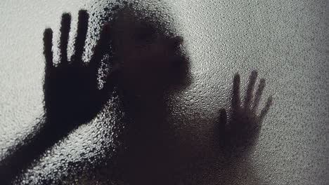 a female silhouette behind the frosted glass moves slowly
