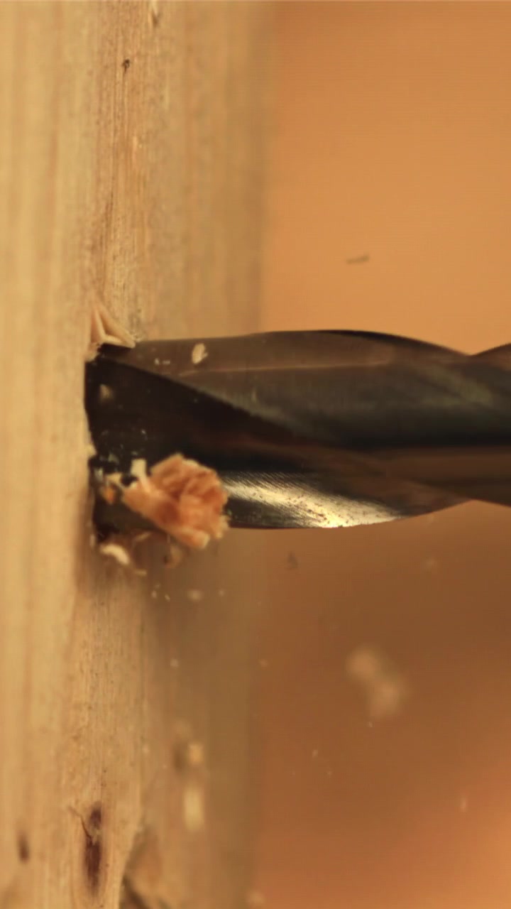 Primo piano di una punta da trapano che fora il legno con segatura che vola