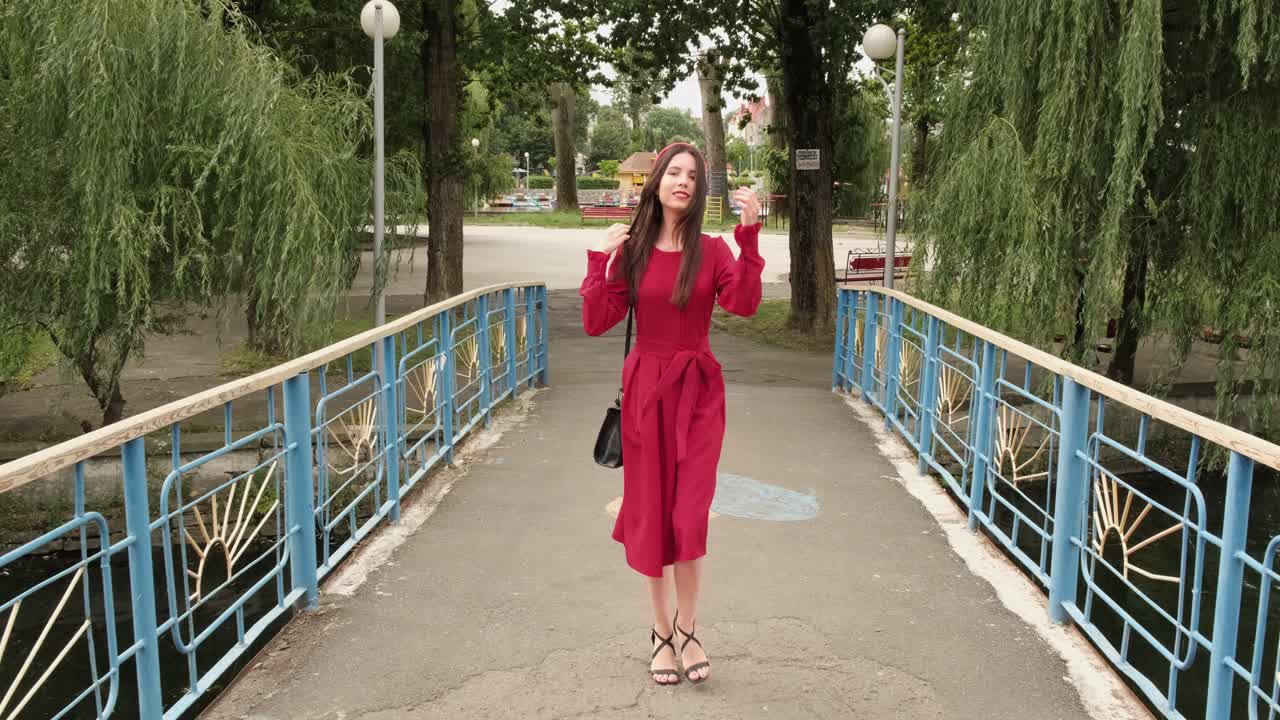 赤い服を着た優雅なブルネットの女性が橋を渡り、公園を散歩している。
