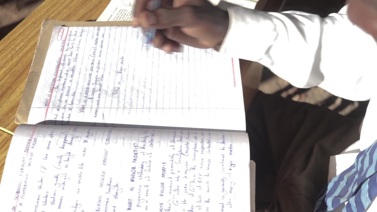 un tiro giratorio en cámara lenta mirando hacia abajo a un joven africano escribiendo notas en su libro escolar
