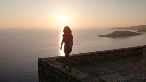 hermosa dama caminando en un mirador con vistas a la costa de montenegro sobre la parte superior de sveti stefan durante una hermosa puesta de sol