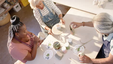 happy diverse group of potters glazing clay jugs and discussing in pottery studio