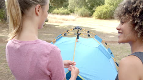 two women assemble a tent in a grassy outdoor setting