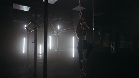 woman-is-climbing-rope-in-gym-training-alone-in-dark-empty-fitness-hall-in-evening