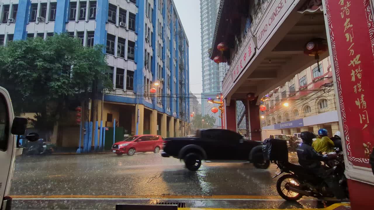 Wide view of cars and scooter motorcycles driving through the rainy streets of Binondo Chinatown, Manila, Philippines. -static shot
