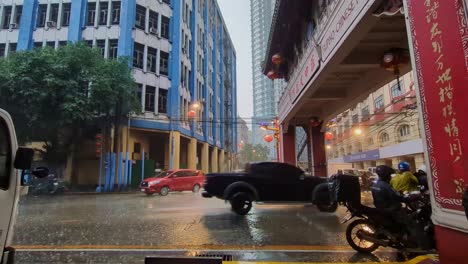 wide view of cars and scooter motorcycles driving through the rainy streets of binondo chinatown, manila, philippines. -static shot