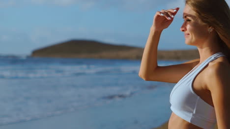 una mujer con ropa deportiva viene al océano y mira a la distancia tocando su cabello después de un entrenamiento en la isla. cámara de cámara lenta