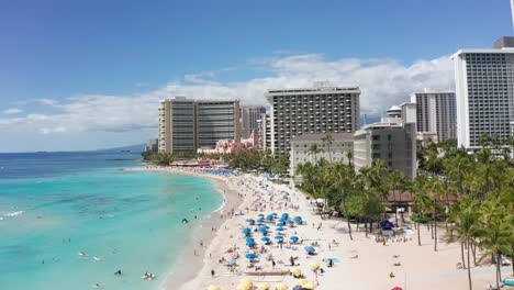 low aerial shot flying over bustling waikiki beach on the island of o'ahu, hawaii