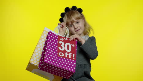 Child-girl-showing-Up-To-30-percent-Off-inscription-sign-and-shopping-bags.-Teen-pupil-smiling