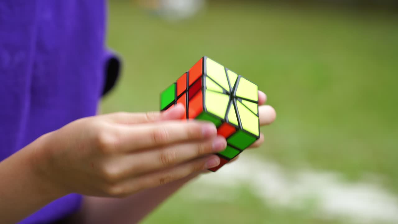 Rubik's cube in boy's hands on blurred background. Clever child brainstorms his mind while solving an intelligent game with cube. Concept of problem solving.