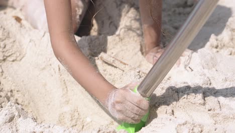 little girl digs hole with big baby shovel on sandy beach