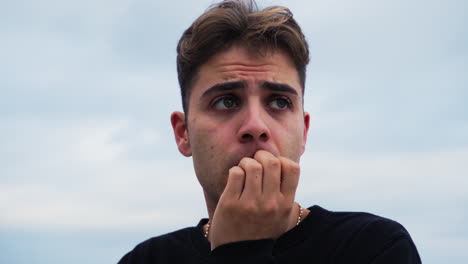 intimidated boy bites his nails cloudy outside in nature