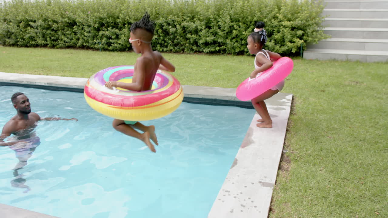 Happy family of an African American man and boy play in a pool at home while a girl jumps in