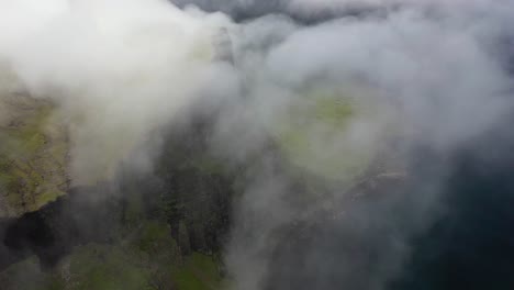 escarpado litoral de las islas feroe a través de las nubes del mar, alta vista aérea de pájaros
